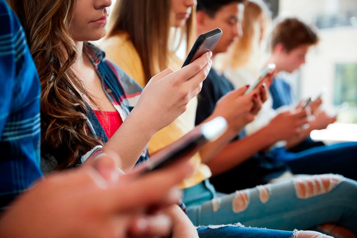 Un gruppo di adolescenti seduti in fila, ciascuno concentrato sul proprio smartphone