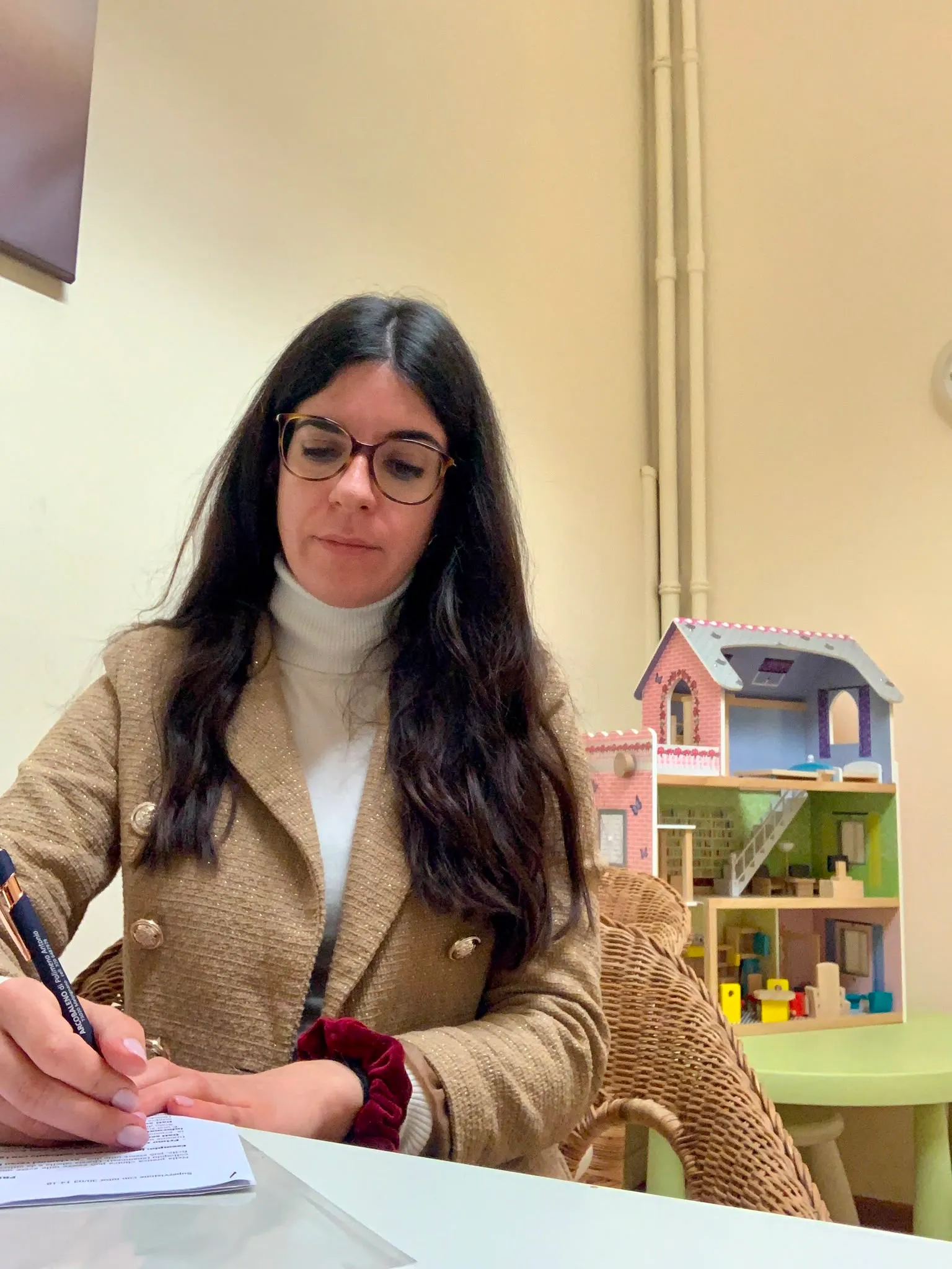 Laura Galati alla scrivania del suo studio, mentre prende appunti; sullo sfondo una casa delle bambole